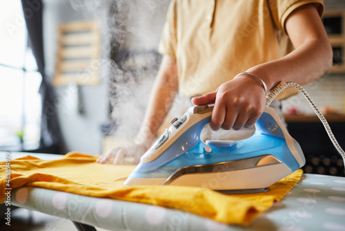 Close up of unrecognizable young woman ironing clothes at home, simple lifestyle and household chores concept, copy space photo