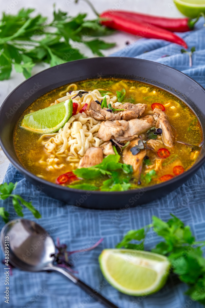 Curry soup with noodles and chicken. Thai chicken green curry paste noodle soup with vegetables and herbs on grey background. Authentic recipe. Selective focus.