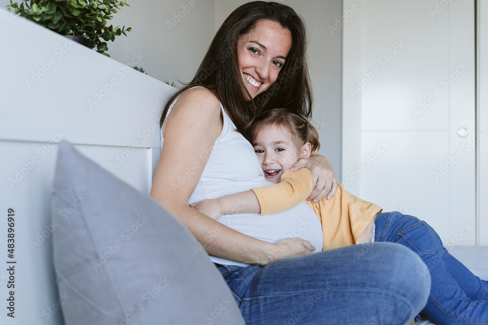 Cute girl hugging happy pregnant mother on bed at home Cute girl hugging happy pregnant mother on bed at home