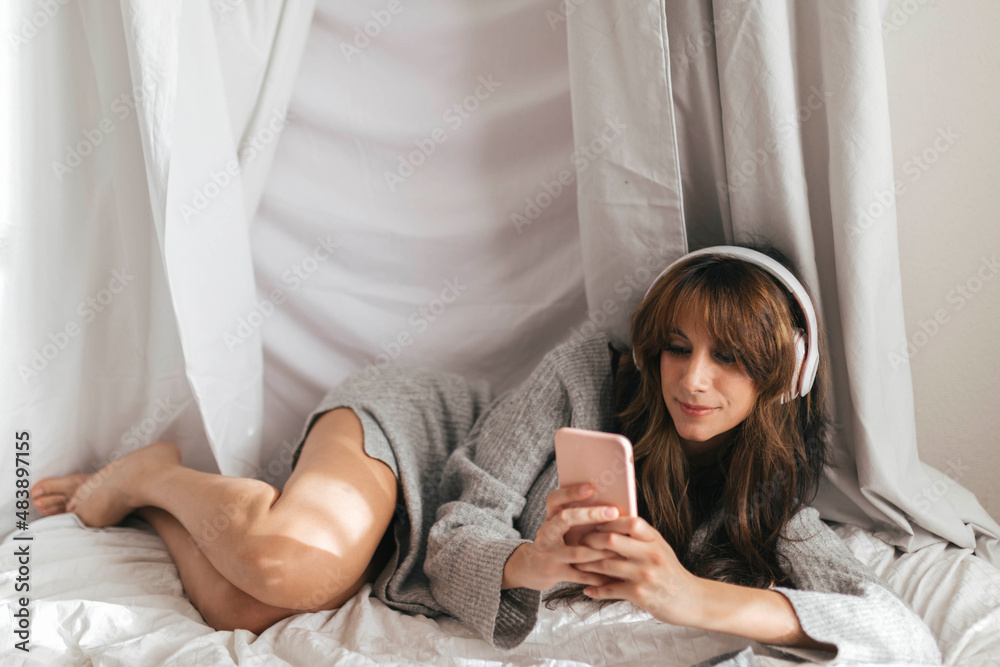 Woman with headphones using smart phone lying in front of backdrop Woman with headphones using smart phone lying in front of backdrop