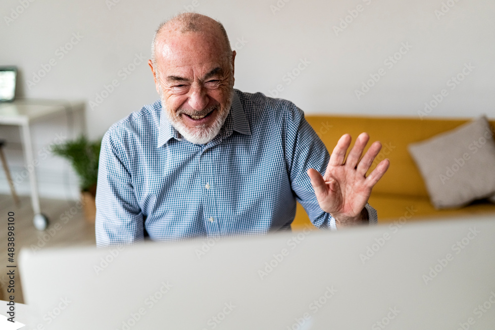 Cheerful freelancer waving hand on video call through desktop computer at home office Cheerful freelancer waving hand on video call through desktop computer at home office