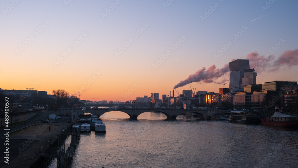 bridge of Tolbiac over the Seine river with chimney smoke of a plant behind at sunset