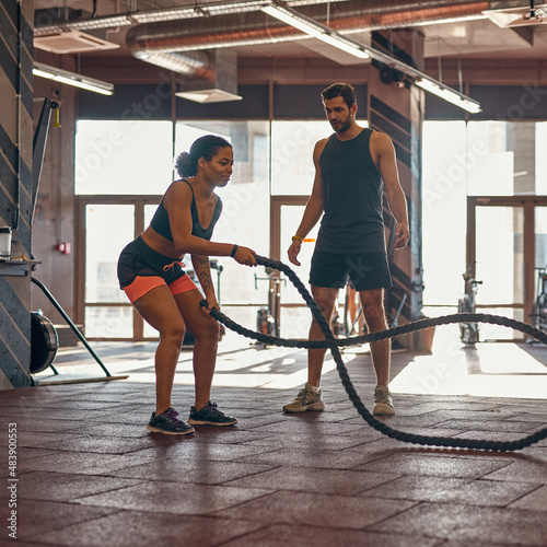 Man look at girl exercise with sports rope in gym