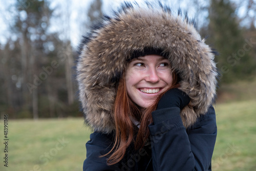 Smiling young woman with warm fur hooded coat looking away in nature photo