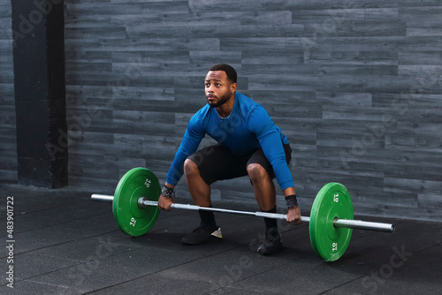 Determined athlete lifting barbell in front of wall at gym