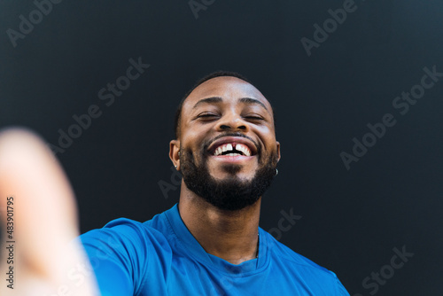 Cheerful athlete with gap teeth taking selfie against black background