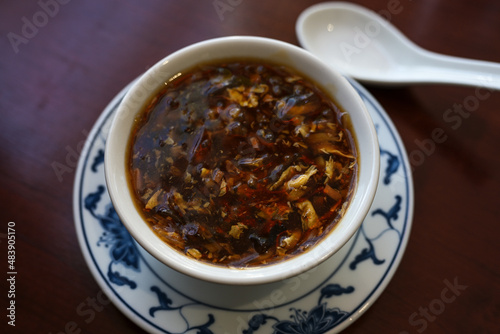 Chinese soup spicy and sour in a bowl with porcelain spoon on a brown table, selected focus