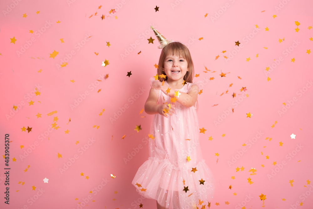 happy child girl in dress having fun with confetti and celebrating her birthday on pink background
