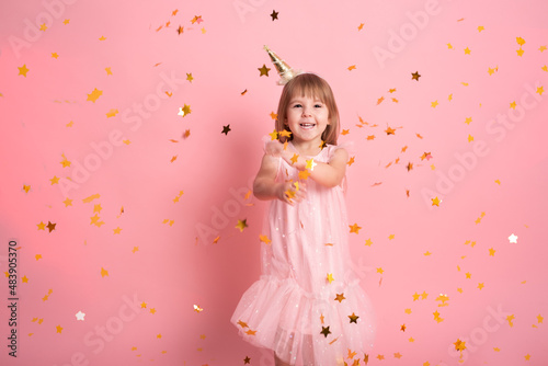 happy child girl in dress having fun with confetti and celebrating her birthday on pink background
