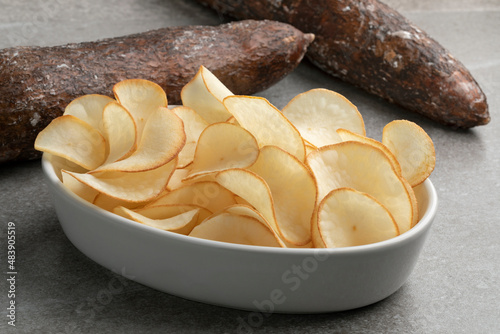 Bowl with deep fried cassava chips close up and waxed cassave tuber in the background  photo