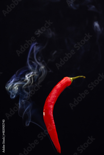 Red hot chili peppers against a black background with smoke coming from it, depicting it to be smoking hot. High quality photo
