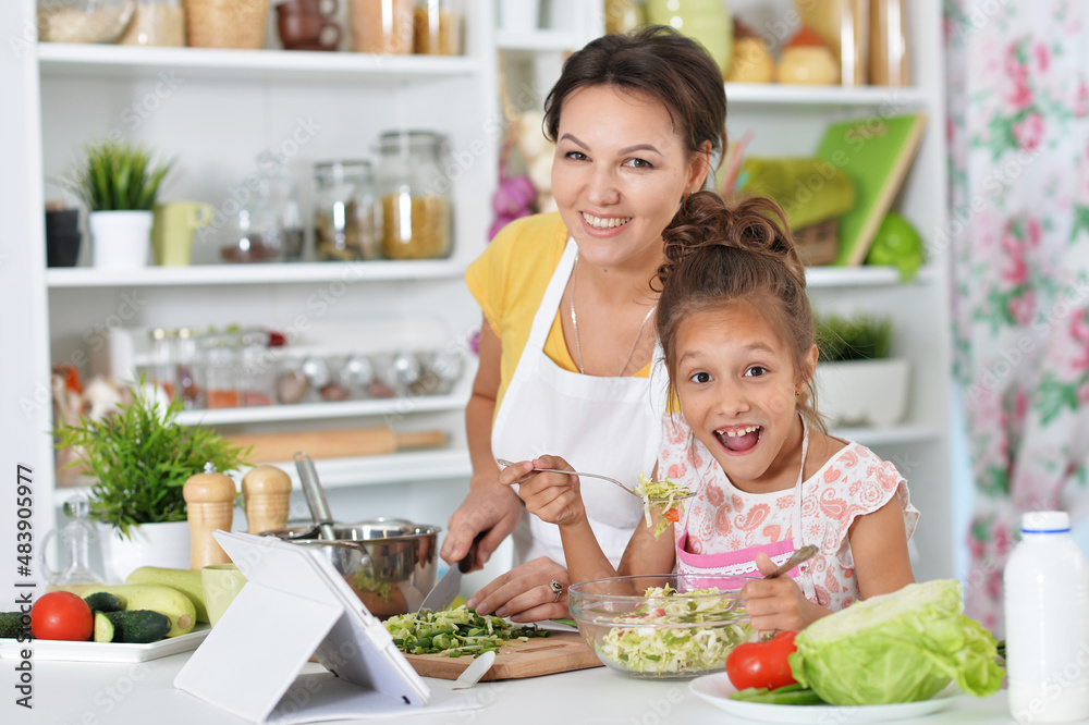 Cute little girl with her mother cooking together at kitchen table Cute little girl with her mother cooking together at kitchen table