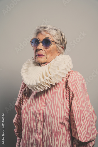 Beautiful and elegant old influencer woman. Cool grandmother posing in studio wearing fashionable clothes. Happy senior lady celebrating and making party. Concept about seniority and lifestyle