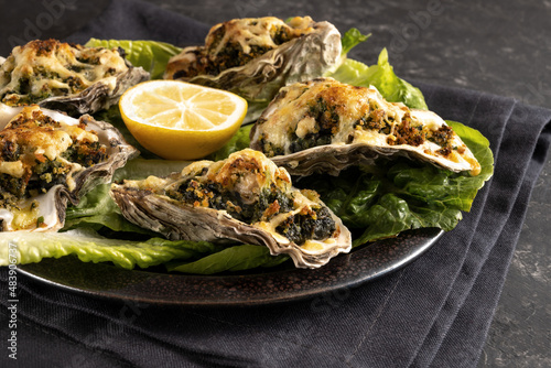 Oysters Rockefeller baked with spinach and cheese, served on a dark plate with lemon and lettuce, selected focus photo