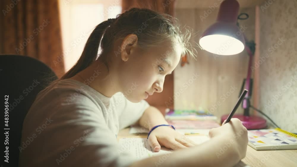 Education concept. Cute smart school child girl writing doing homework sit at home table. Teen girl doing school assignment. Happy child studying at home in the evening. Education concept. Cute smart school child girl writing doing homework sit at home table. Teen girl doing school assignment. Happy child studying at home in the evening.