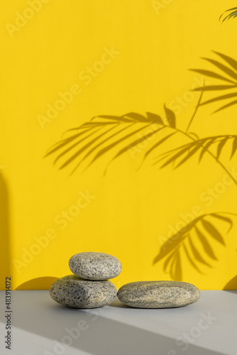 Podiums made of stones on a gray table on a yellow background with a shadow from the leaves of a palm tree. Showcase for product promotion  beauty  natural eco cosmetic.