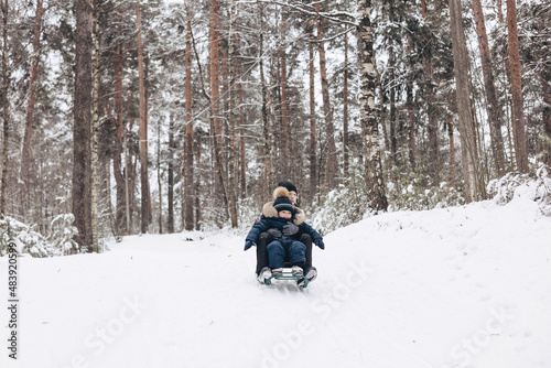 Two joyful boys sledding and having fun together. Happy children playing in snow in winter forest. Brothers spending time together