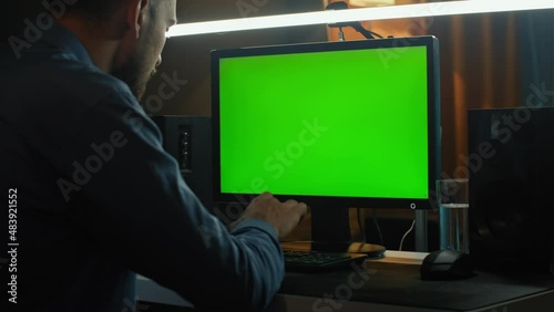 A man works in front of a computer with a green screen.