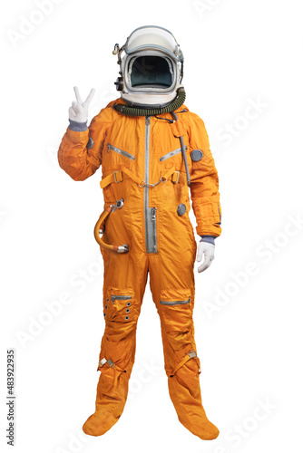 Astronaut wearing an orange spacesuit and helmet showing hand victory sign gesture isolated on white background. Unrecognizable cosmonaut with a hand victory sign