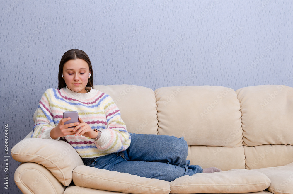 Young teen girl resting on a couch, using smartphone digital device at home. Texting, social media, online shopping. Young teen girl resting on a couch, using smartphone digital device at home. Texting, social media, online shopping.