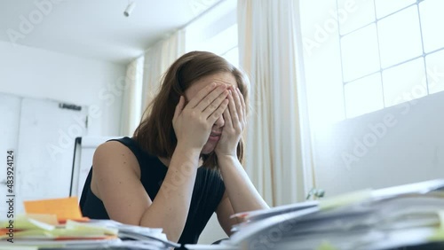 Stressed woman and coworker in office feeling sad and having headache about the pile of paper work she must finish. Concept: Stressed employee at her messy desk