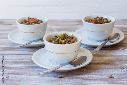 Lentil and escarole soup served in white cups on white wooden background