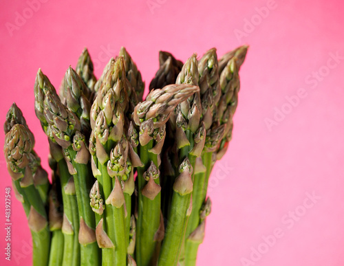 a bunch of green young raw asparagus on a pink background. green low-calorie vegetable, rich in vitamins. spring seasonal vegetables