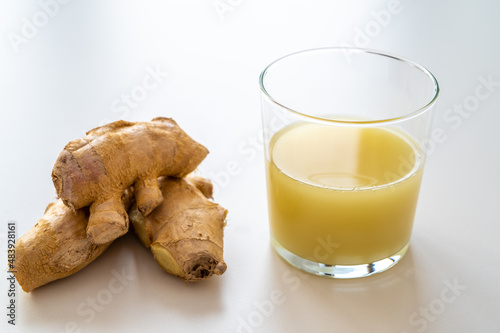 Ginger root, with pieces of ginger next to it and a glass of ginger juice.  photo