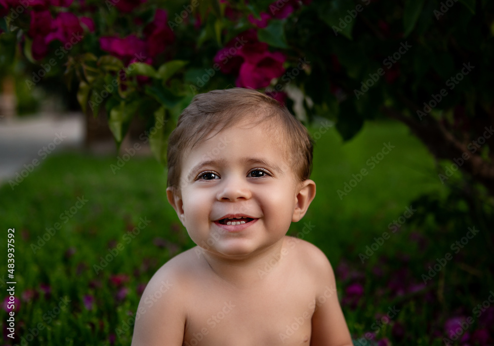 Baby boy's smilly portrait in garden under the bush with flowers Baby boy's smilly portrait in garden under the bush with flowers