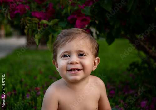 Baby boy's smilly portrait in garden under the bush with flowers