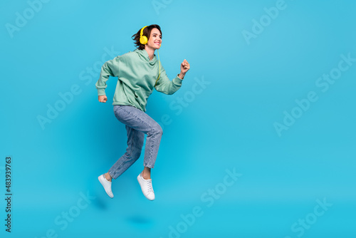 Full length profile photo of cute millennial brunette lady run wear headphones pullover jeans footwear isolated on blue background