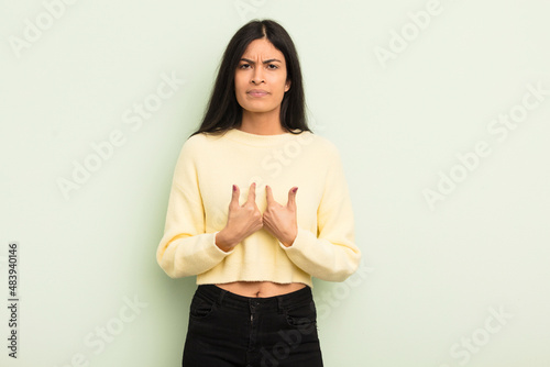 hispanic pretty woman pointing to self with a confused and quizzical look, shocked and surprised to be chosen photo
