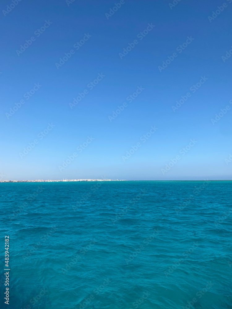 Fototapeta premium The sea is azure. Sand island on the horizon. Light wave. The outlines of the city on the horizon. 