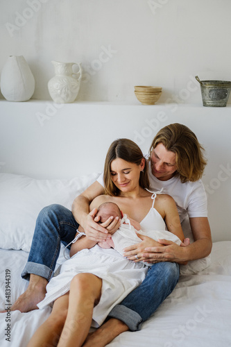 A young mother breastfeeds a newborn girl sitting next to her husband.