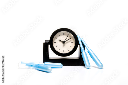 Cuatro tampones con aplicador azul junto a un reloj de mesa negro sobre fondo blanco. Concepto de hora de la menstruación