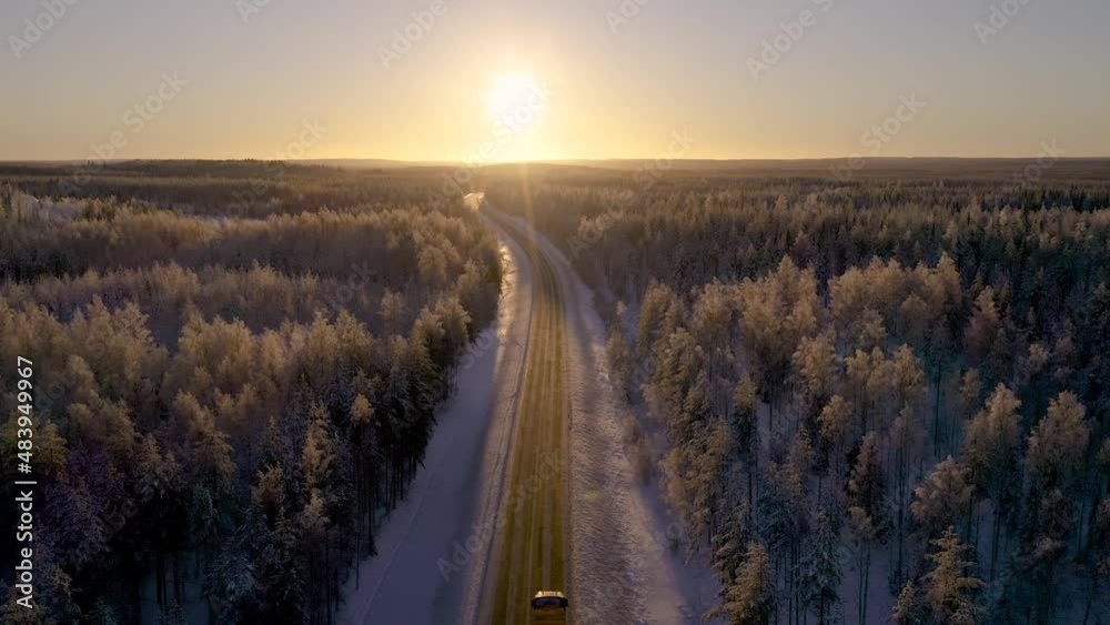 Aerial view of cargo truck on road driving towards golden sunset in winter in nordic country. Freight transportation concept.