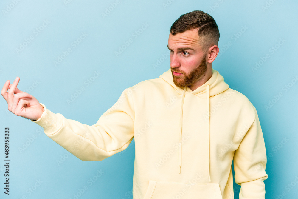 Young caucasian man isolated on blue background pointing with finger at you as if inviting come closer. Young caucasian man isolated on blue background pointing with finger at you as if inviting come closer.