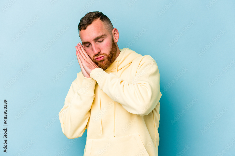 Young caucasian man isolated on blue background yawning showing a tired gesture covering mouth with hand. Young caucasian man isolated on blue background yawning showing a tired gesture covering mouth with hand.