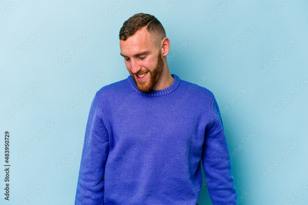Fototapeta premium Young caucasian man isolated on blue background laughs and closes eyes, feels relaxed and happy.