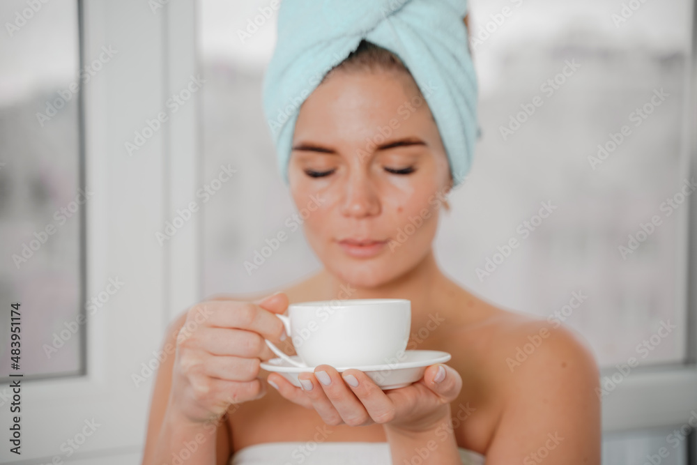Young serene relaxed woman in spa bath towel drinking hot beverage tea coffee after taking shower bath at home. Beauty treatment, hydration concept. Young serene relaxed woman in spa bath towel drinking hot beverage tea coffee after taking shower bath at home. Beauty treatment, hydration concept.