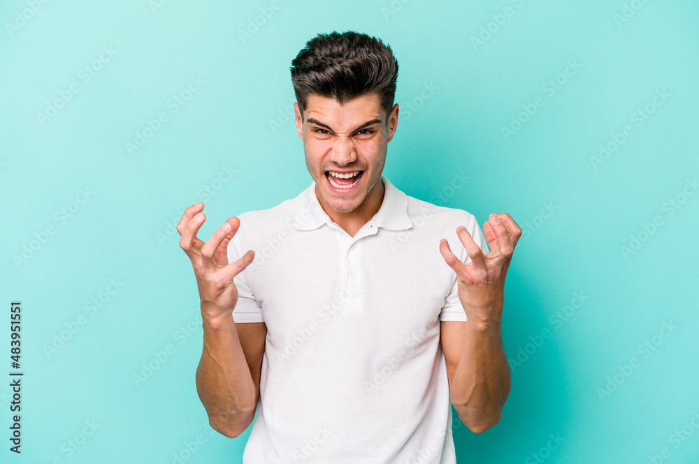 Young caucasian man isolated on blue background screaming with rage. Young caucasian man isolated on blue background screaming with rage.