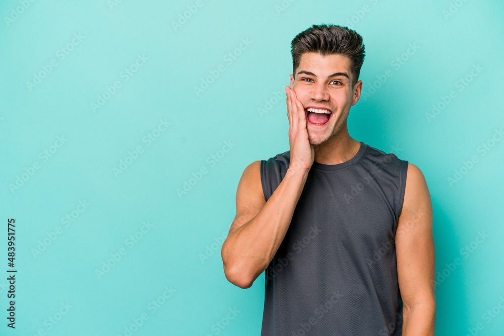 Young caucasian man isolated on blue background shouts loud, keeps eyes opened and hands tense.