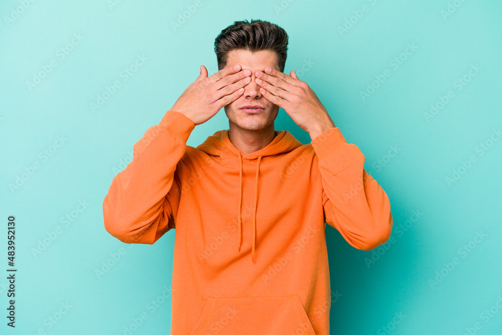 Young caucasian man isolated on blue background afraid covering eyes with hands. Young caucasian man isolated on blue background afraid covering eyes with hands.