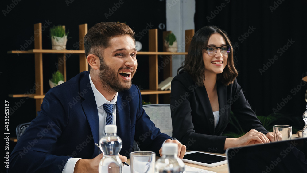 young businessman laughing near smiling colleague in meeting room