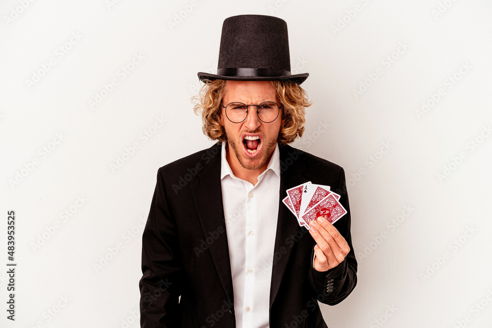 Young magician caucasian man holding magic cards isolated on white background screaming very angry and aggressive. Young magician caucasian man holding magic cards isolated on white background screaming very angry and aggressive.