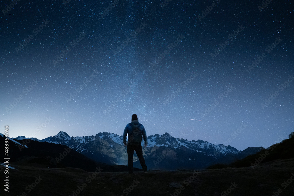 man standing under th night sky looking to the mountains