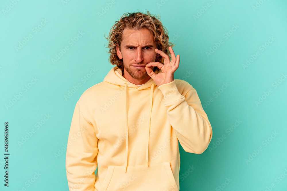 Fototapeta premium Young caucasian man isolated on blue background with fingers on lips keeping a secret.