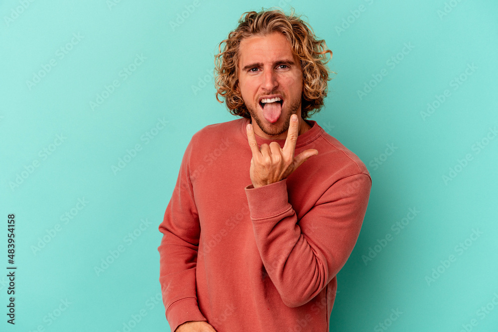 Young caucasian man isolated on blue background showing rock gesture with fingers