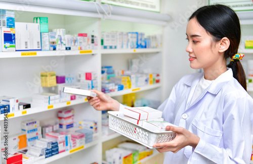 Pharmacist chemist woman standing refills the shelves with new stocks in pharmacy drugstore photo