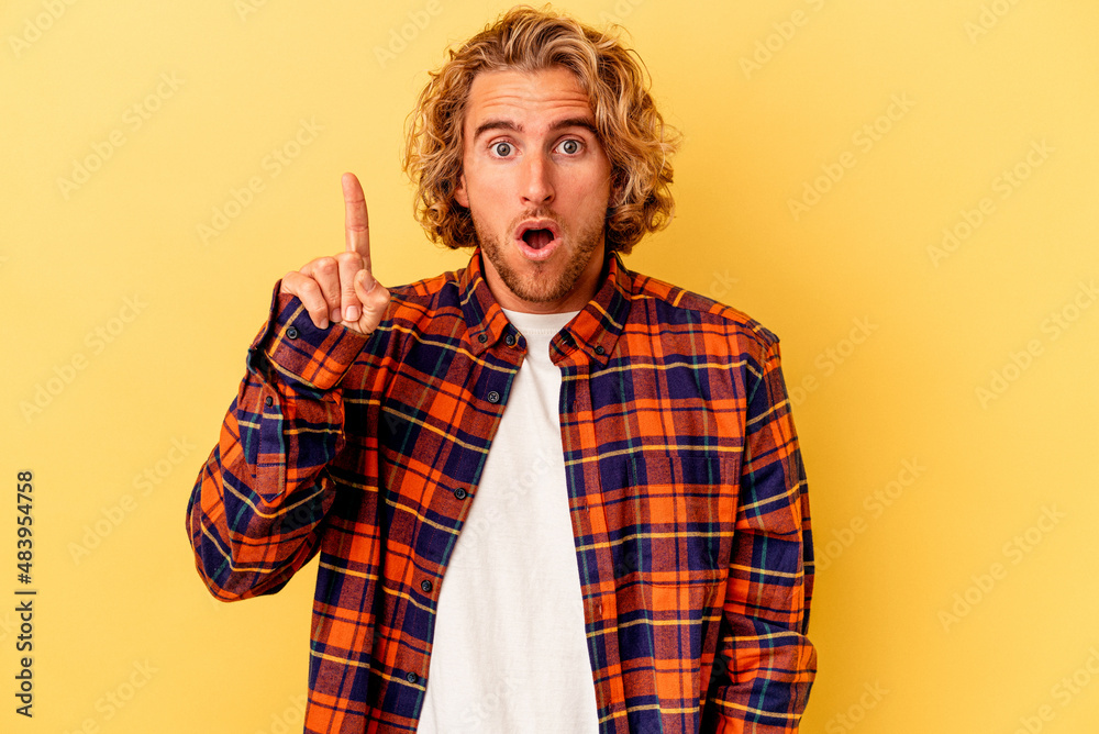 Young caucasian man isolated on yellow background pointing upside with opened mouth.